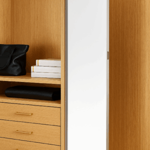 Modern bedroom with beige bedding, wall mirror, and built-in white shelves.